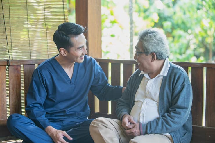 Aged care support worker sitting and talking with an elderly man outdoors