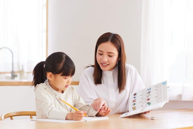 Early childhood educator helping a young child with schoolwork at a table