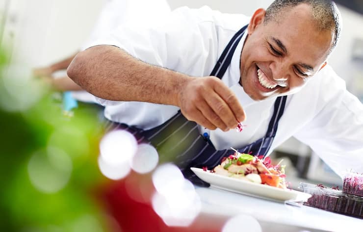 Smiling chef plating a fresh salad in a professional kitchen